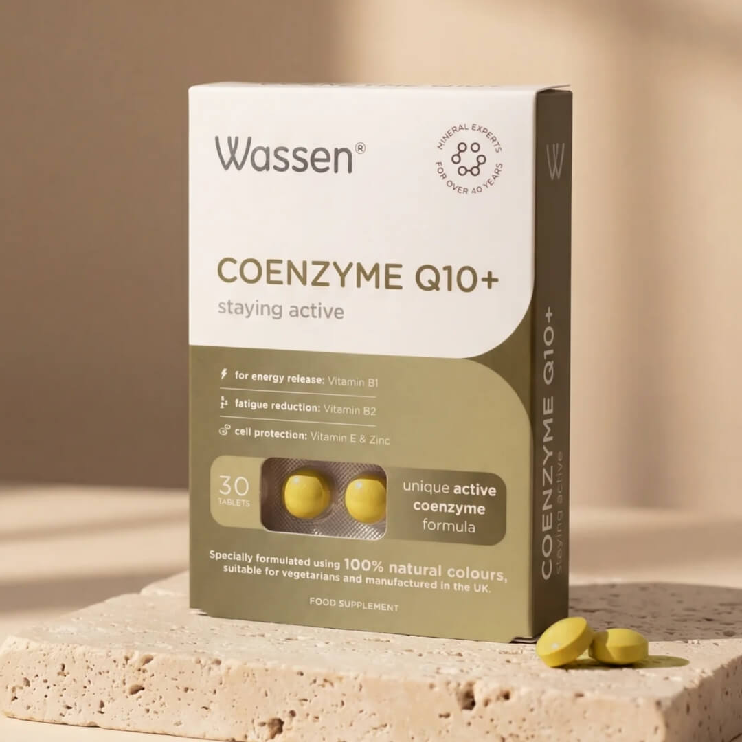 Wassen Coenzyme Q10+ food supplement box in a warm beige and olive-green color scheme, displayed on a textured stone pedestal with three yellow tablets in front.