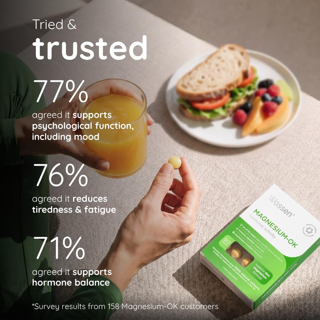 A person holds a glass of orange juice and a single magnesium supplement tablet, with a green and white Vassen Magnesium-OK box placed nearby on a tabletop. A sandwich and fruit are visible in the background.